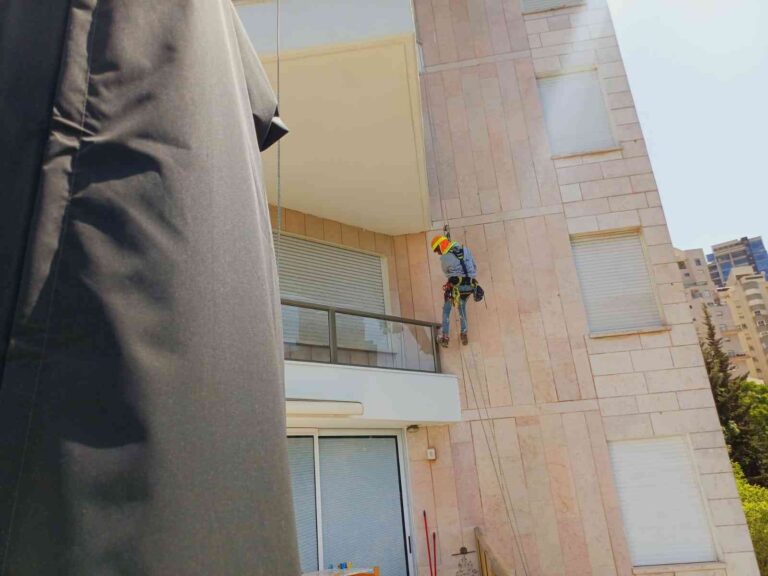 עובד מבצע תיקונים בקיר חוץ של בניין בעבודה בגובה (סנפלינג)
